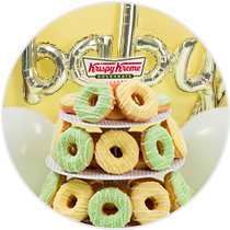 A doughnut tower with yellow iced and green iced doughnuts surrounded by party decorations